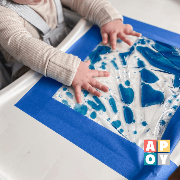 baby in high chair playing with oil and water sensory bag taped to tray