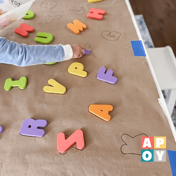 child hand reaching on to brown craft paper on table with colorful foam letters