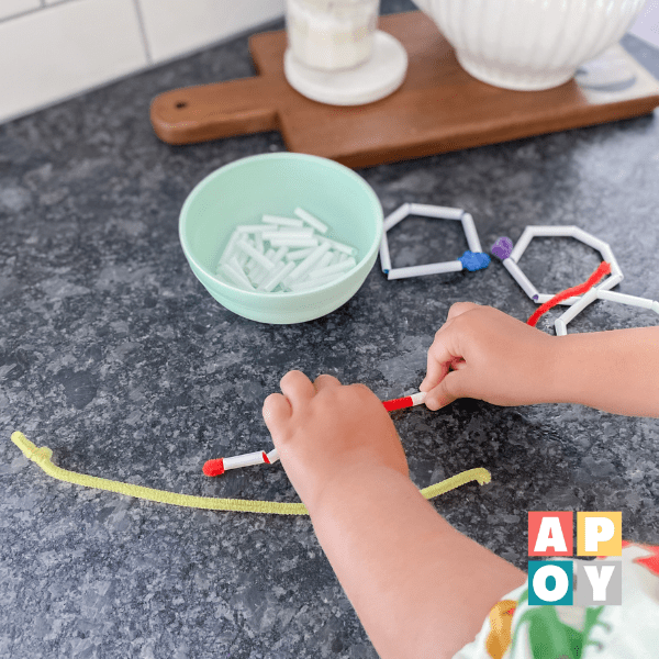 child hand threading straw pieces on pipe cleaner