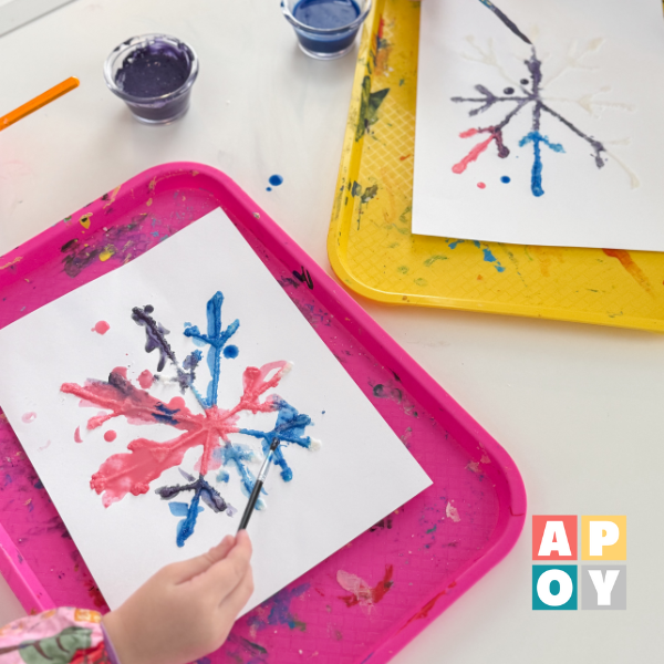 childs hand holding paintbrush over salt snowflake art