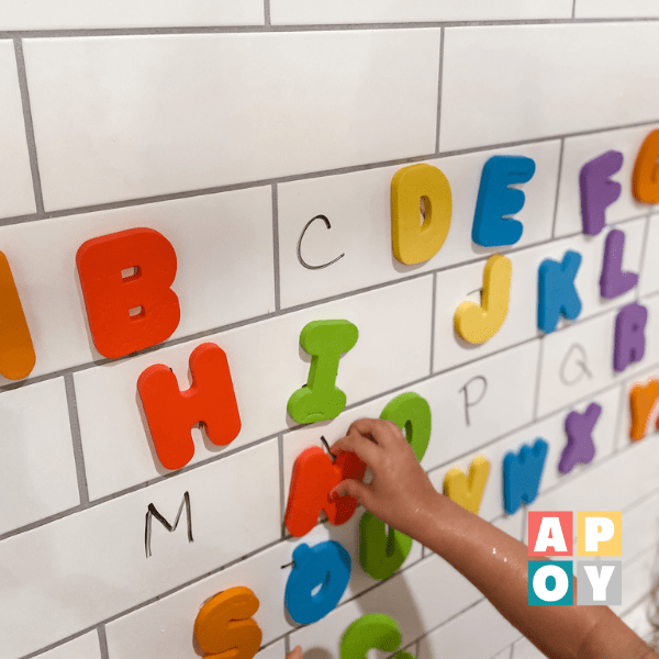 childs hand putting colorful foam letters on bathroom tub wall