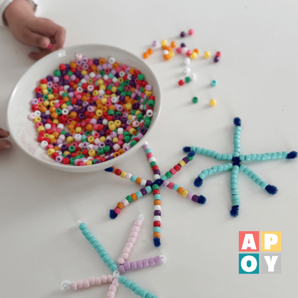 childs hand with bowl of colored beads making bead snowflakes