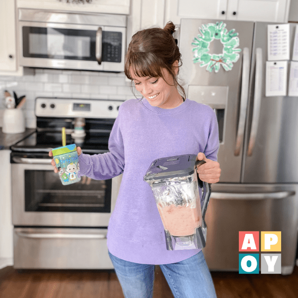 woman holding blender with smoothie and cup in kitchen