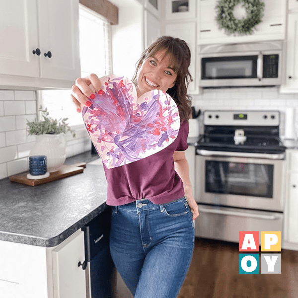 woman holding painted heart craft in kitchen