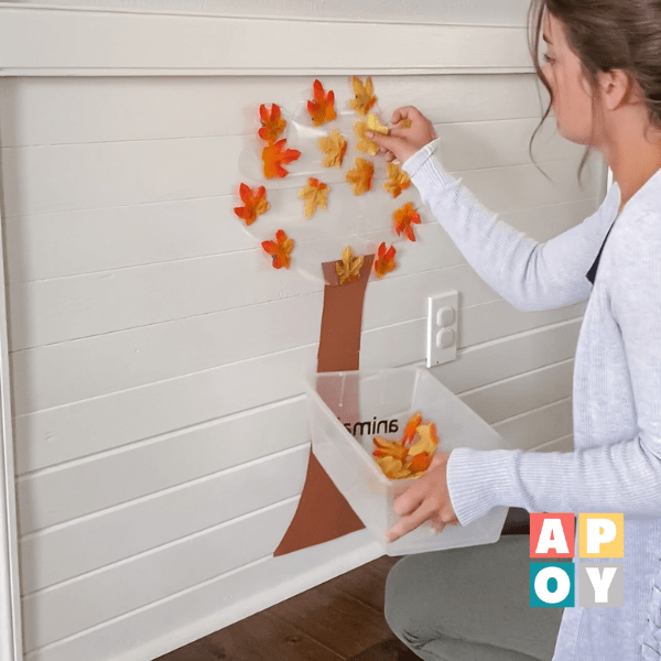 woman putting faux leaf on contact paper taped to wall