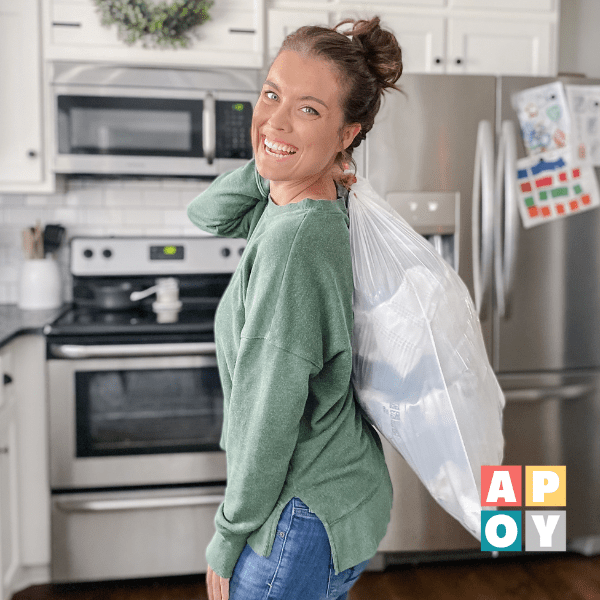 woman standing in kitchen holding white trash bag over her shoulder